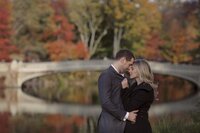 Central park engagement photos, Deborah Zoe Photography. A couple embrace in front of Bow Bridge in Central Park.