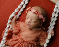 Newborn baby in a lace dress and floral headband resting on a red backdrop. Photographed by Inland Empire newborn photographer Kaitlyn Dawn Photography.