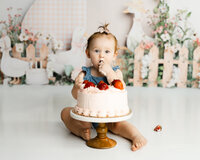 Baby exploring a strawberry birthday cake during a playful cake smash session. Photographed by Yucaipa baby photographer Kaitlyn Dawn Photography.