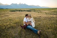 Couple sharing a kiss in a golden field with the Grand Teton mountain range in the background during their Jackson Hole engagement session