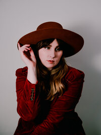 Moody studio portrait of Morgan Wright wearing a hat against a dark red backdrop.