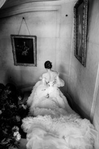 Elegant black and white bridal portrait of a bride descending a curved staircase in a dramatic ruffled gown, captured in a timeless fine art wedding setting with classic framed artwork.