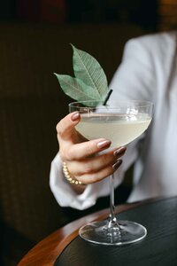 Coupe cocktail with a leaf garnish on a dark bar table