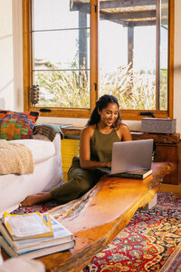 Woman working on a laptop on the living room floor in afternoon light