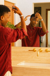 Man checking his hair in the bathroom mirror, hair care vertical