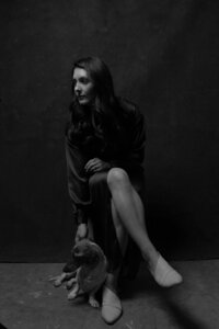 Shadowed headshot of Sarah sitting in a chair with her dachshund, Waylon, at her feet