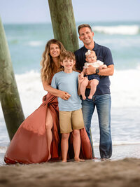 Family of four standing together under a pier during a beach portrait session in Eastern North Carolina
