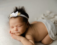 Sleeping newborn baby girl wearing a delicate headband and posed on a soft neutral blanket during a studio newborn photography session with newborn photographer Kaitlyn Dawn Photography.