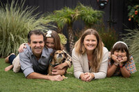Family of four with a dog posing in a laying down position in their backyard for family photos