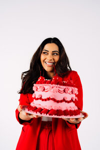 Founder smiling while holding a red and pink cake during her personal brand photography session.