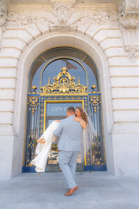 groom carries bride in front of san francisco city hall wedding
