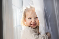Toddler playing in curtain, smiling and laughing