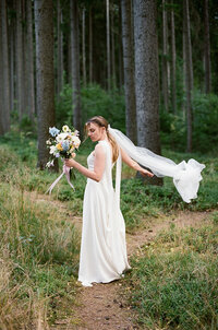 Ethereal bride in a flowing wedding dress posing in a dreamy pine forest, captured on film.
