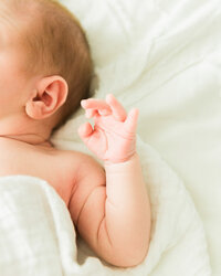 Close-up detail photo of a newborn baby’s tiny hand and arm wrapped in soft fabric during an in-home newborn session.