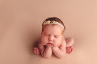 Iconic froggy pose of a newborn baby with soft peach tones and floral headband, photographed in a professional Lake Country photo studio.