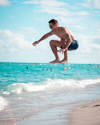 David jumps above the waves at a sunny tropical beach