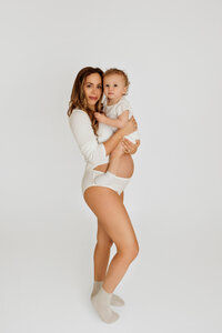 mother-to-be in neutral tones posing with her young child during timeless studio maternity session
