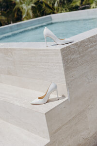 A bride's white wedding shoes displayed in a chic, carefree way next to a pool at a wedding in Tulum
