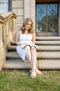 High school senior girl sitting on outdoor steps reading a book, Inland Empire lifestyle senior portrait captured by Kaitlyn Dawn Photography.