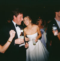 Bride and groom laughing and dancing together at their wedding reception at Burritt on the Mountain, surrounded by guests holding drinks.