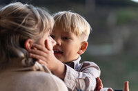 Son holding mom's face while telling her a secret