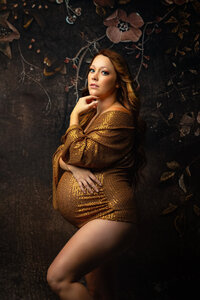 Pregnant mother wearing a sequenced gold suit poses during her fine art maternity session in Minnesota.