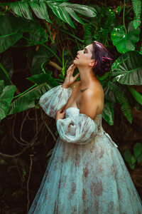 Woman with dark purple hair poses against the green foliage at Hollis Gardens wearing a puff sleeved gown in Lakeland Florida