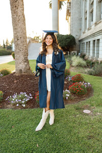 High school graduate wearing cap and gown standing on a grassy lawn outside a school building, graduation portrait by Kaitlyn Dawn Photography.
