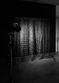 Black-and-white behind-the-scenes view of a photography studio set with lighting equipment and curtains.