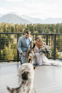 A newlywed couple crouching down as two dogs run towards them.