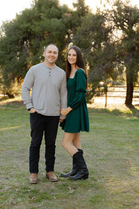 Smiling couple standing side by side in a grassy field during golden hour, outdoor lifestyle portrait captured by Kaitlyn Dawn Photography.