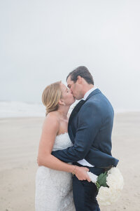 The bride and groom hold each other close, their faces softly pressed together as they kiss