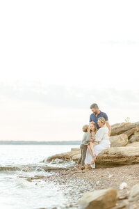 Family photo of them all sitting on a large rock by a Dallas Fort Worth lake for their family photos.