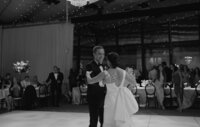 couple in black suit and wedding dress dancing together in wedding ballroom