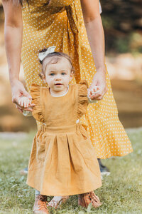Toddler girl in a yellow dress reaching up outdoors during a Cleveland family photography session