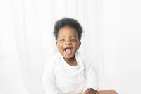 baby boy wearing white shit, laughing during cake smash photoshoot in Franklin Tennessee photography studio