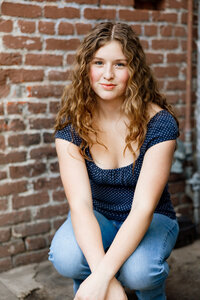 High school senior girl sitting against a brick wall in natural light, urban senior portrait session by Kaitlyn Dawn Photography, professional senior photographer.
