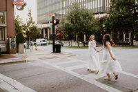 lesbian couple running down street together in white dresses