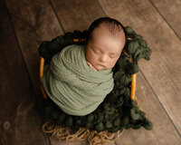 Sleeping newborn baby wrapped in a green swaddle and posed on a textured blanket during a studio newborn photography session with newborn photographer Kaitlyn Dawn Photography.