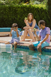 Three kids with ice cream on the edge of the pool in summer