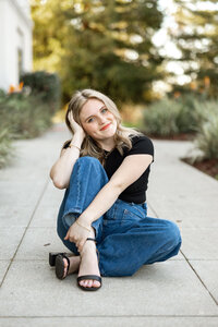High school senior girl sitting on a sidewalk with a natural background during an outdoor Yucaipa senior portrait session with Kaitlyn Dawn Photography.