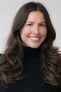 young woman with dark hair smiling while wearing a dark sweater posed for a modeling headshot