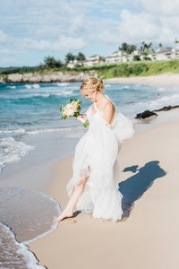 Bride touches the ocean with her toes on her wedding day.