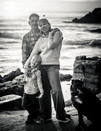 Black and white image of a family posing on the beach near sunset