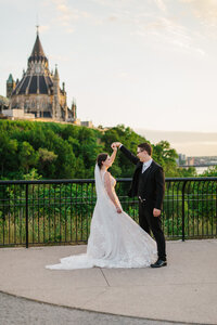 Groom spinning bride in front of a hilly landscape with an ornate building