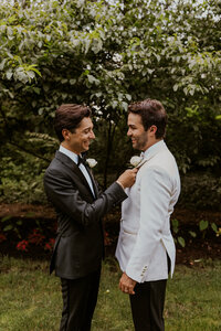 Wedding day portrait featuring two grooms in formal attire sharing a candid moment in a garden setting.