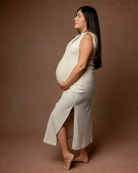 Side profile of a pregnant woman in a beige maternity dress, gently holding her baby bump during a session by Kaitlyn Dawn Photography in the Inland Empire.