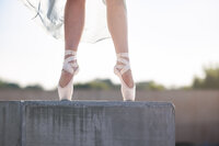 The feet of a ballerina are seen on point standing atop a concrete wall. The skyline is white behind her.