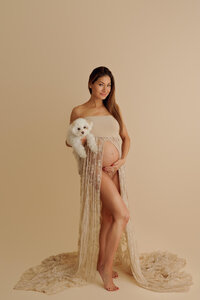 expecting mother in gown revealing baby bump holding her dog during artistic studio Los Angeles maternity portrait