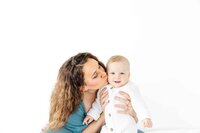 mother-kissing-baby-smiling-in-white-outfit